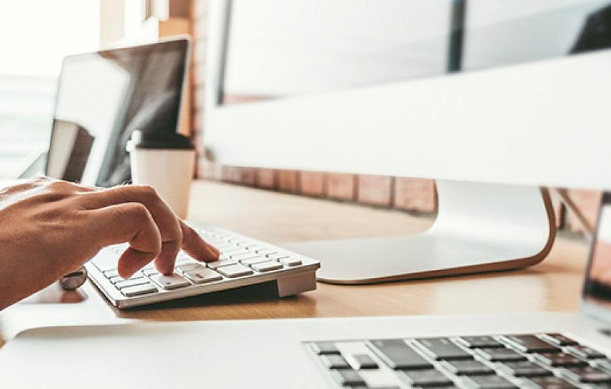 Man typing at a desktop Mac computer with a laptop and IPad nearby